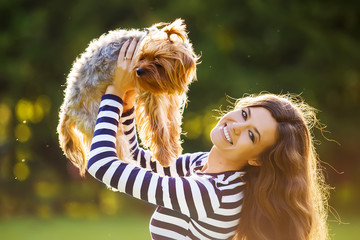 Beautiful girl in a striped sweater smiles and holds a small dog