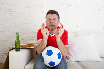 man watching football on tv nervous and excited suffering stress crossing fingers for goal