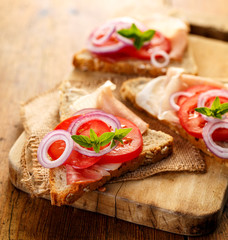 Sandwich with smoked ham, tomato, red onion and fresh oregano on a wooden board