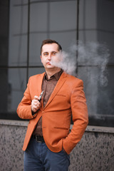 Young man smoking electronic cigarette on background of building