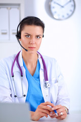 Doctor wearing headset sitting behind a desk with laptop over grey background