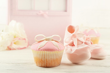 Tasty cupcake with bow and baby shoes, decorative baby carriage on color background