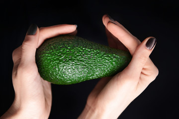 Female hands holding avocado on black background