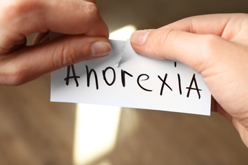 Female hands cutting piece of paper with word anorexia