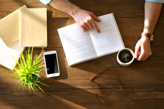 Young man reading book and drinking coffee at the table