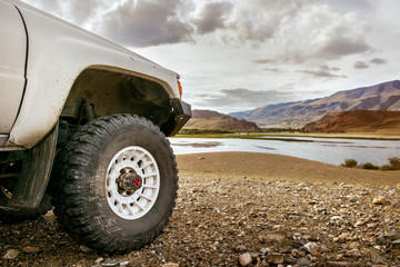 Fototapeta na wymiar Big SUV car wheel stands on backdrop of mountain lake