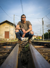 Attractive young man sitting on railroad