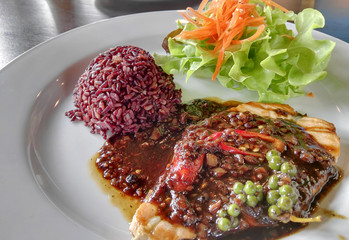 Fish fried and black pepper sauce served with a rice of healthy and salad on the white dish,Soft focused