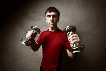 Fototapeta na wymiar Muscle man posing with dumbbells on gray wall backdrop