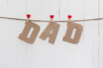 Cardboard letters DAD hanging on clothespins on a white wooden b