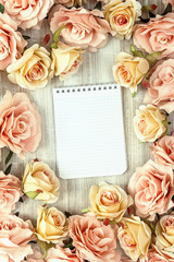 Background with rose flowers and empty notebook for text on wood