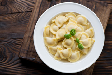 Ravioli in bouillon, top view, rustic wooden background