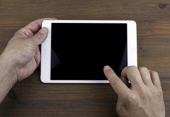 Hands of a man holding blank tablet device over a wooden workspa