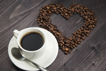A cup of black coffee and coffee beans in the shape of a heart on a wooden table
