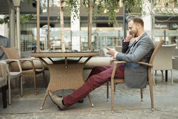 Businessman sitting at outdoor cafe, speaking by cellphone and smile