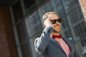 Sytlish businessman in sunglasses using smartphone at city downtown