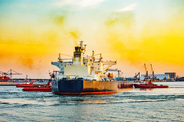 Fototapeta premium Big ship with escorting tugs leaving port at sunset.