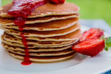 Pancakes with fresh strawberry and jem  on white plate on white wooden background  in garden or on nature background.  Stack of pancakes on the table. Closeup.