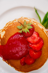 Top view of pancakes with fresh strawberry and jem on white plate.  Stack of pancakes on the table.