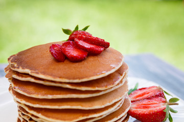 Pancakes with fresh strawberry and mint on white plate on pink wooden background  in garden or on nature background.  Stack of pancakes on table.