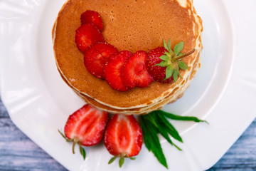 Top view of pancakes with fresh strawberry and mint on white plate on wooden background.