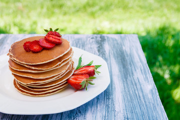 Pancakes with fresh strawberry and mint on white plate on pink wooden background  in garden or on nature background.  Stack of pancakes on table.