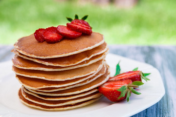 Pancakes with fresh strawberry and mint on white plate on pink wooden background  in garden or on nature background.  Stack of pancakes on table.