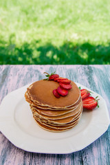 Pancakes with fresh strawberry and mint on white plate on pink wooden background  in garden or on nature background.  Stack of pancakes on table.