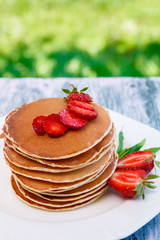 Pancakes with fresh strawberry and mint on white plate on pink wooden background  in garden or on nature background.  Stack of pancakes on table.