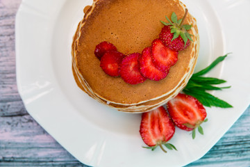 Pancakes with fresh strawberry and mint on white plate on blue wooden background. Top view.