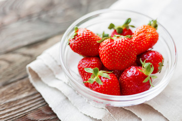 Fresh juicy strawberries in glass bowl. Rustic background with homespun napkin.