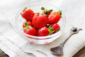 Fresh juicy strawberries in glass bowl. Rustic background with homespun napkin and vintage spoon.