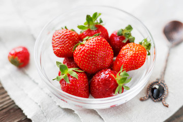 Fresh juicy strawberries in glass bowl. Rustic background with homespun napkin and vintage spoon.