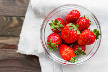Fresh juicy strawberries in glass bowl. Rustic background with homespun napkin. Top view.