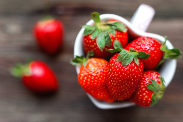 Fresh juicy strawberries in cup shaped as a heart, symbol of love. Rustic wooden background. Top view, place for text.
