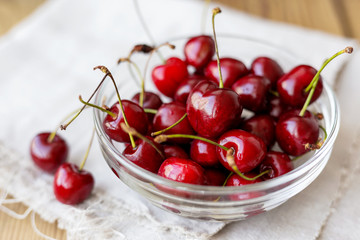 Fresh juicy sweet cherries in glass bowl. Rustic background with homespun napkin.