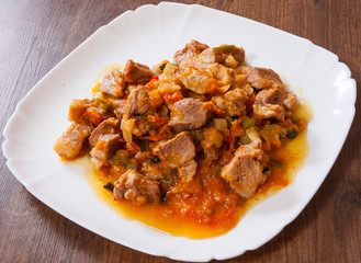Stewed meat with vegetables in a plate on wooden table