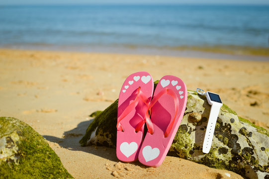 Flipflops and smart watch on sandy ocean beach vacation concept, top view flat lay style