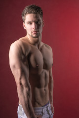 Fototapeta premium Handsome young and attractive man, male model. Shirtless male model against a red background.