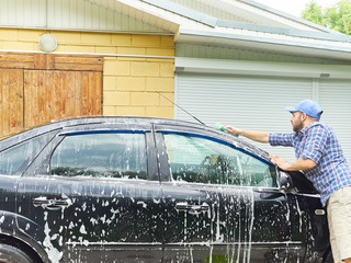 Man washing his black car near house.