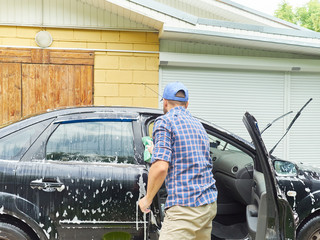 Man washing his black car near house.