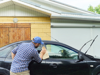 Man washing his black car near house.