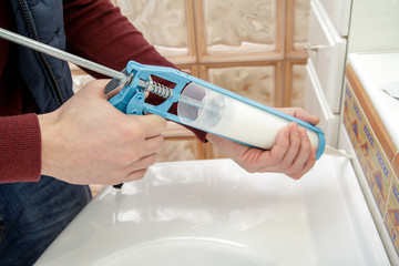 Worker hands applying silicone sealant with caulking gun.