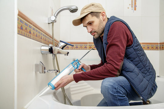 Man applying silicone sealant with caulking gun in the bathroom.