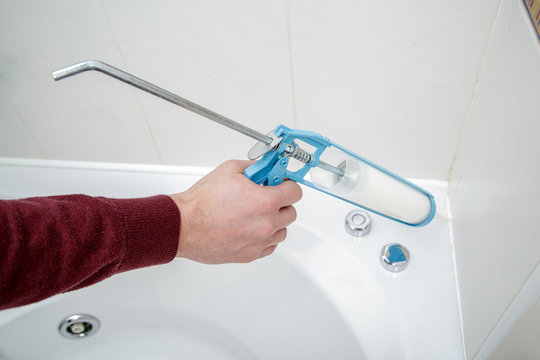 Plumber hand applying silicone sealant with caulking gun in the bathroom.