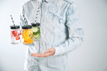 Waiter offers three cold refreshment beverages from strawberry,orange,lime,mint,cucumber,ice and sparkling water in rustic jars to drink for sale on camera