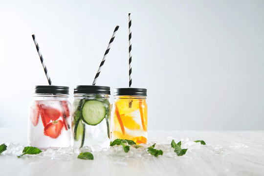 Three cold refreshment beverages from strawberry,cucumber,lime,mint,ice and sparkling water in rustic jars with drinking straws inside,isolated,focus on orange lemonade