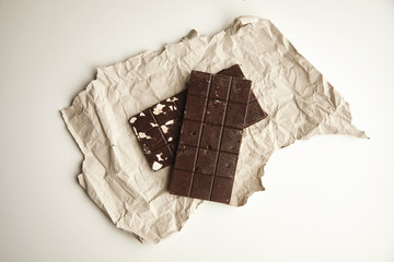 Top view on two different rustic chocolate bars freshly baked , on craft paper, isolated on white table