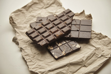 Closeup on three different rustic chocolate bars freshly baked with oats, nuts and cacao beans, on craft paper, isolated on white table, for sale,  top view