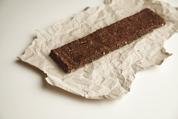 Side view artisan organic freshly baked healthy chocolate bar with berries and grinded nuts on craft paper, isolated on white table